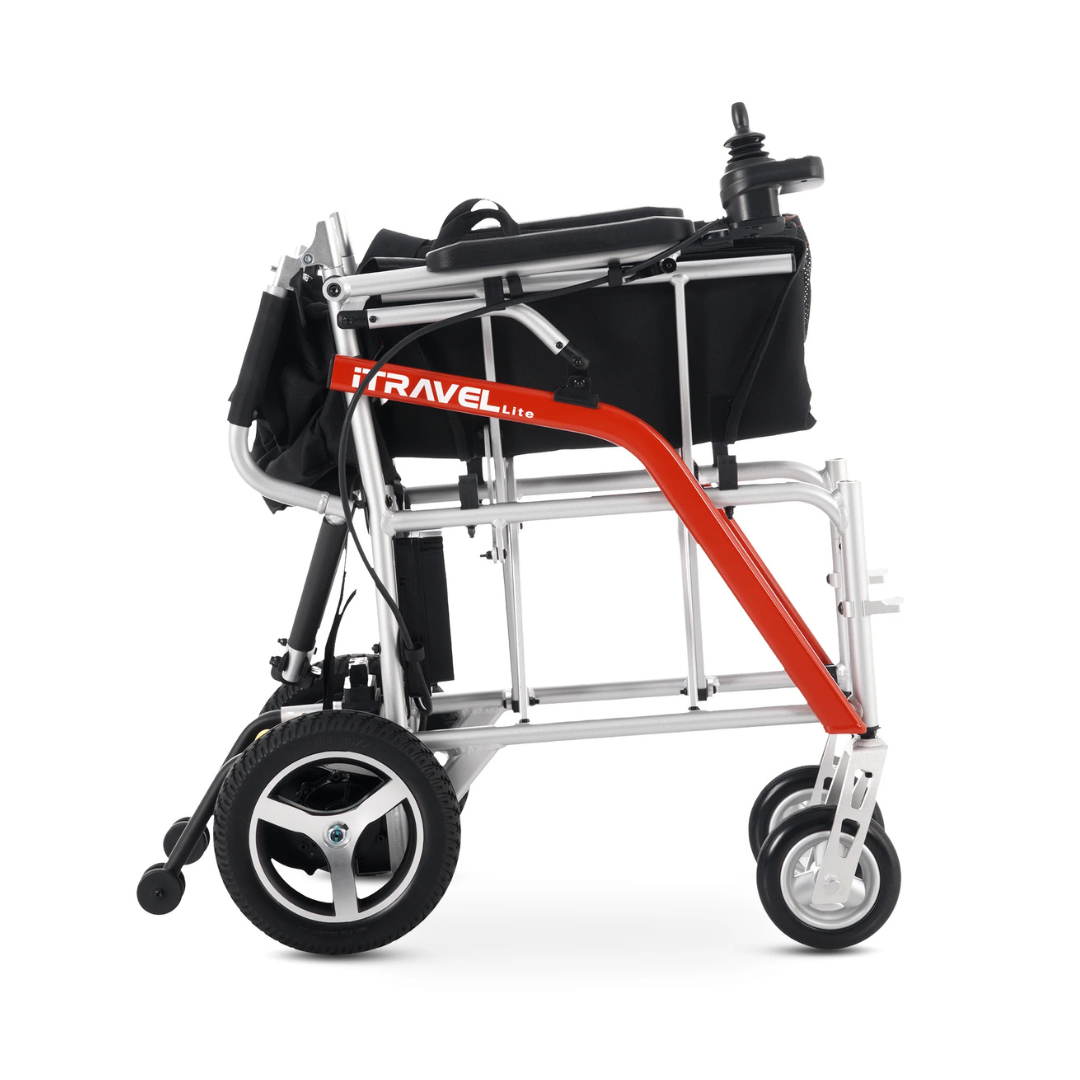 The Metro Mobility iTravel Lite Portable Powerchair features a black seat, silver frame, orange TRAVEL side bar, and large rear wheels. Shown compactly folded for easy transport, it’s ideal for airplane-friendly travel.