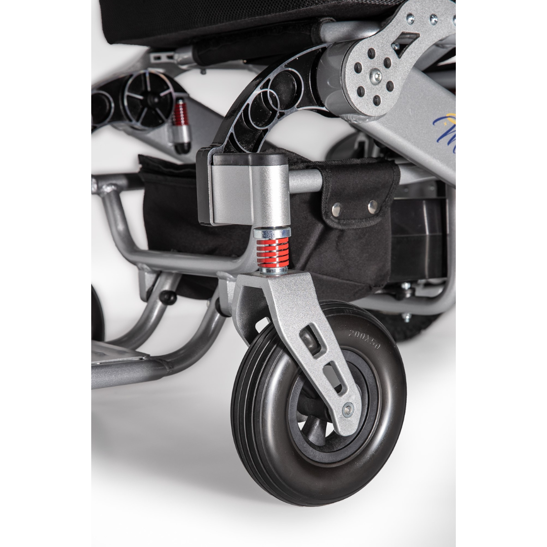 Close-up of the front wheel and suspension on the Miracle Mobility Platinum 8000 Bariatric Portable Powerchair, highlighting a black wheel, red shock absorber, sturdy frame, and a black storage pouch behind it.