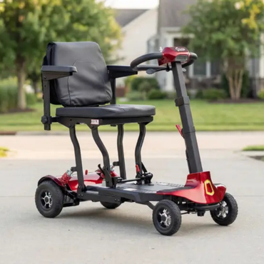 The Monarch Genie Lightweight Portable Scooter features a padded seat, armrests, and four wheels in a red and black design—ideal for comfort and easy mobility on driveways with grass and houses nearby.