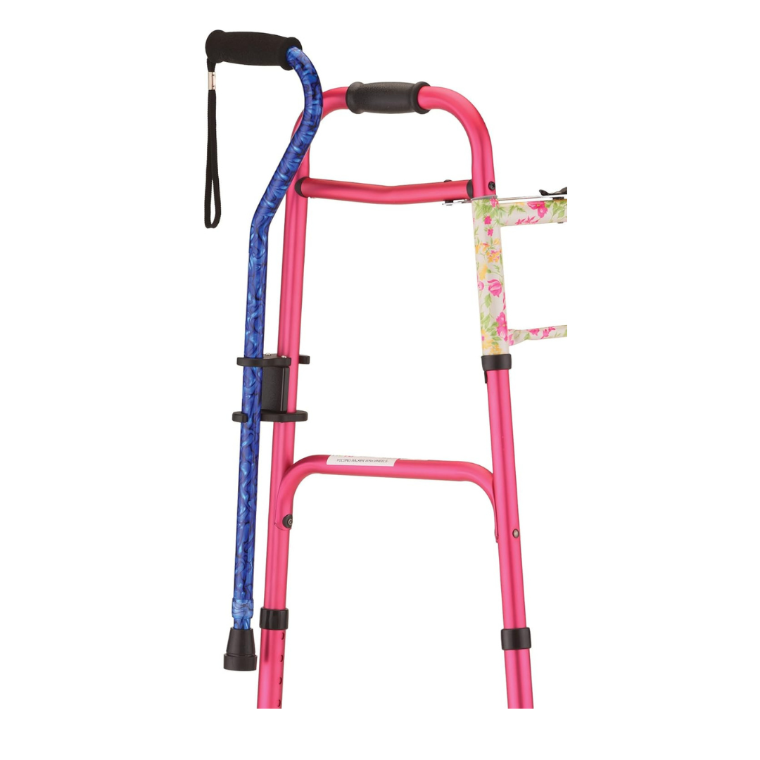 The NOVA Medical Cane Holder for Rollators and Folding Walkers, shown with a pink walker and blue cane, features a floral-patterned clamp to securely hold the cane; both stand upright against a white background.