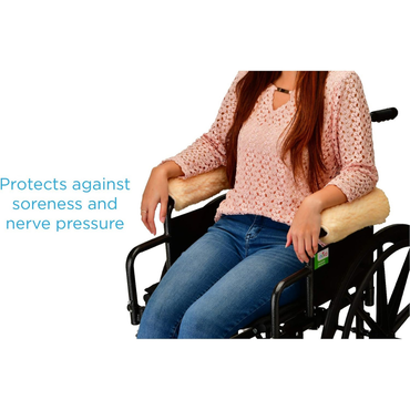 A woman sits in a wheelchair with Nova Sheepskin Fleece Armrest Covers in soft beige. Blue text on the left reads: “Protects against soreness and nerve pressure.”.