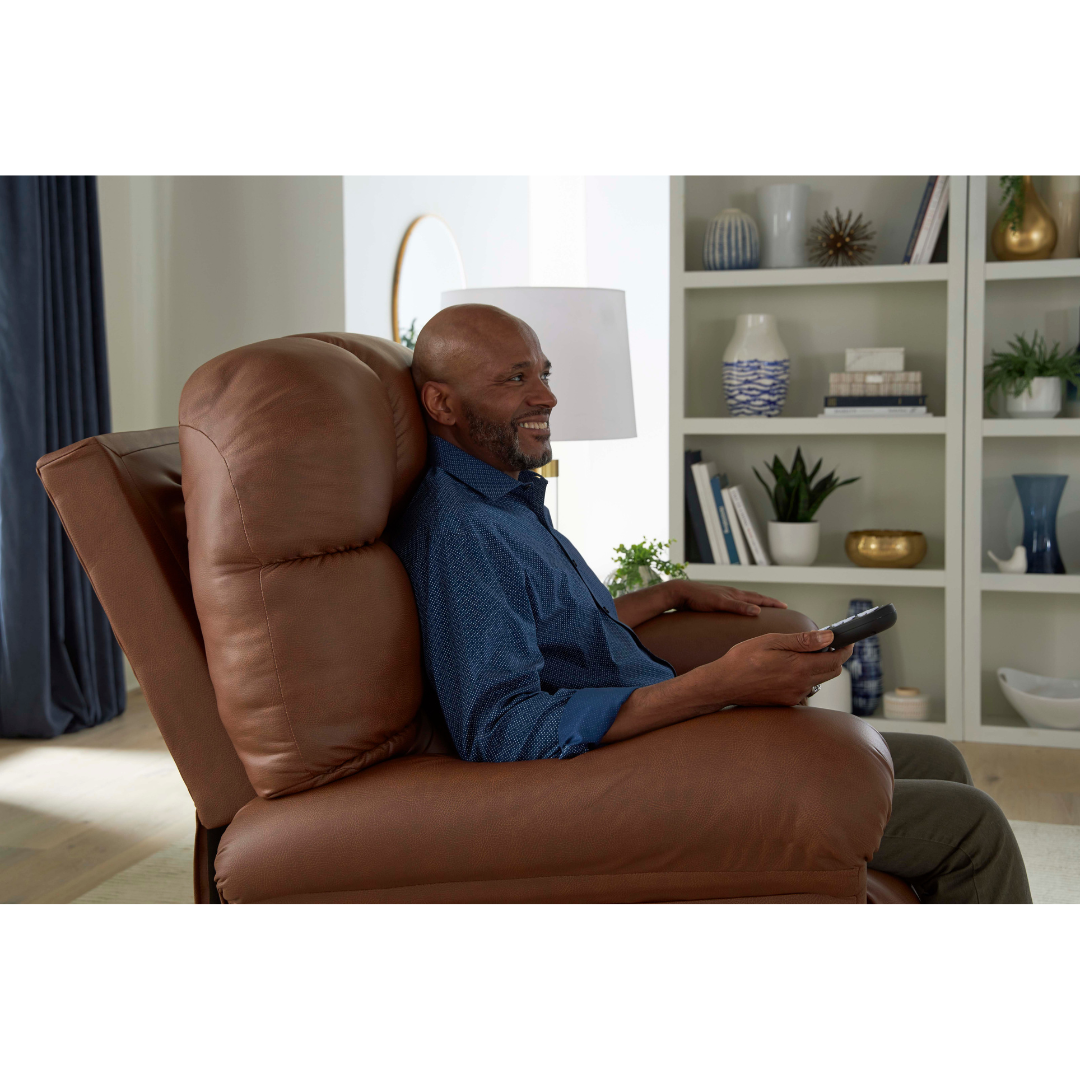 A smiling man relaxes in a Golden Tech PR515 Cloud Recliner With Lift Assist, ZG+ & Twilight, holding a remote in a bright living room with shelves, decor, and plants in the background.