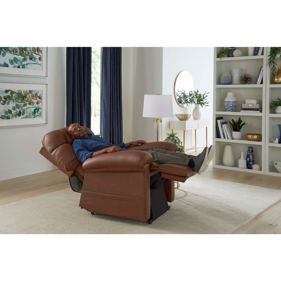 A man relaxes in the Golden Tech PR515 Cloud Recliner With Lift Assist, ZG+ & Twilight, fully reclined in a modern living room featuring light walls, bookshelves, large windows, and framed artwork.