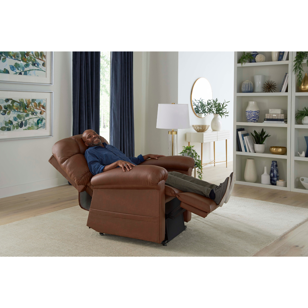 A man relaxes fully extended in a Golden Tech PR515 Cloud Recliner With Lift Assist, ZG+ & Twilight, in a bright living room with white walls, shelves, artwork, and a large window with dark curtains.