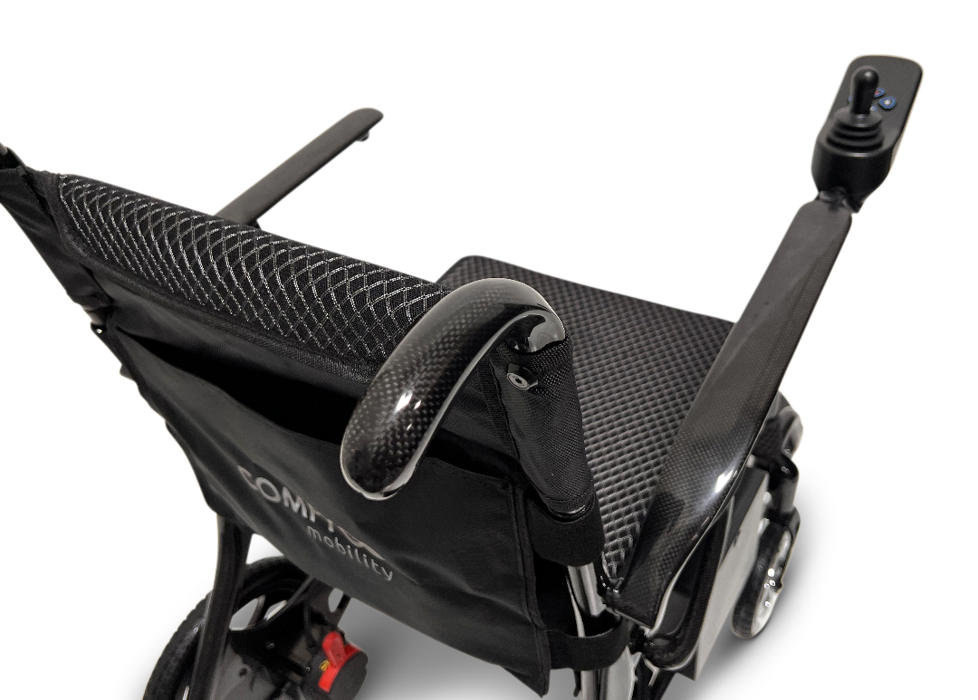 Close-up of the sleek black ComfyGo Phoenix Carbon Fiber Electric Wheelchair, showcasing its fabric seat and backrest. With armrests and a right-side joystick control, it features foldable carbon fiber spokes and displays the COMFY mobility label on the backrest.