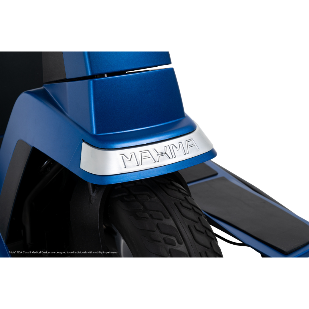 Close-up of a blue Pride Mobility Maxima 3-Wheel Bariatric Scooter with a black tire. A silver plate above the tire is engraved with "MAXIMA." The scooter’s footrest and part of its frame are also visible.