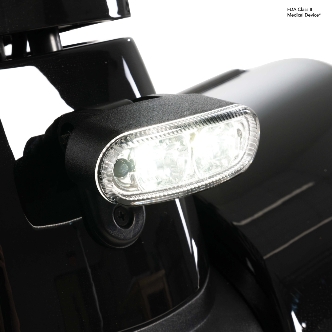 Close-up of a bright LED headlight on the glossy black Pride Mobility Pursuit® 2 Offroad HD Scooter, with an FDA Class II Medical Device label visible in the top right corner.