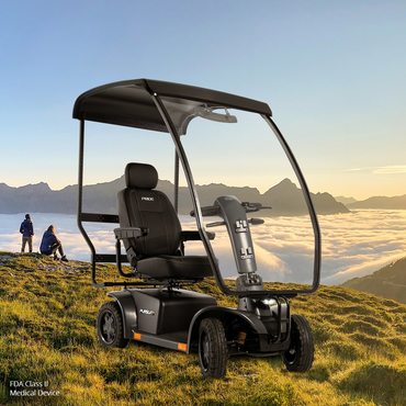 A Pride Mobility Pursuit® 2 Offroad HD Scooter with a canopy is parked on a grassy hilltop at sunrise, where two people sit nearby, enjoying views of clouds and distant mountains under a clear sky.