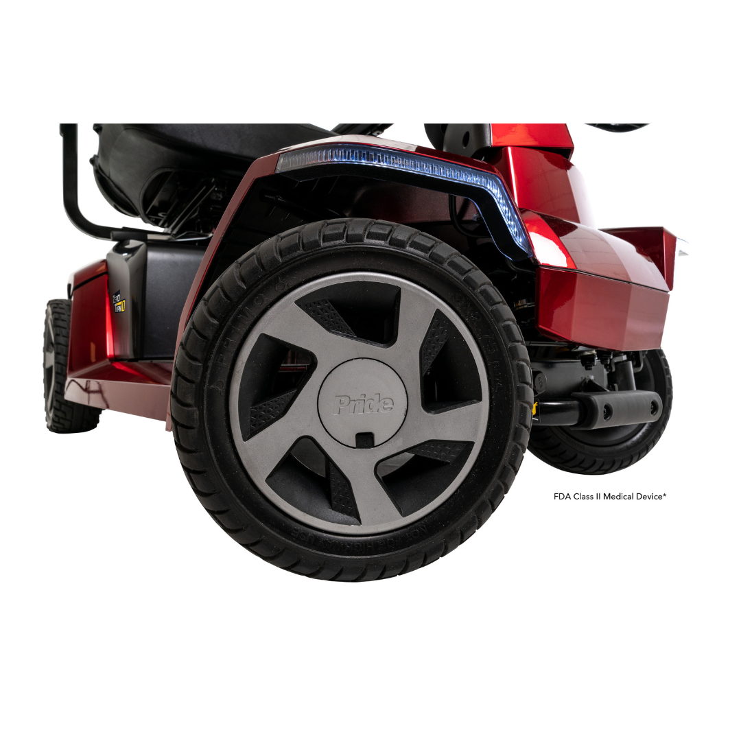 Close-up of the rear wheel and frame of a red Pride Mobility Zero Turn 10 HD Scooter, showing black treaded tires and detailing with the Pride logo on the hub. This midsize scooter features advanced EZ Turn Technology for tight maneuvering.