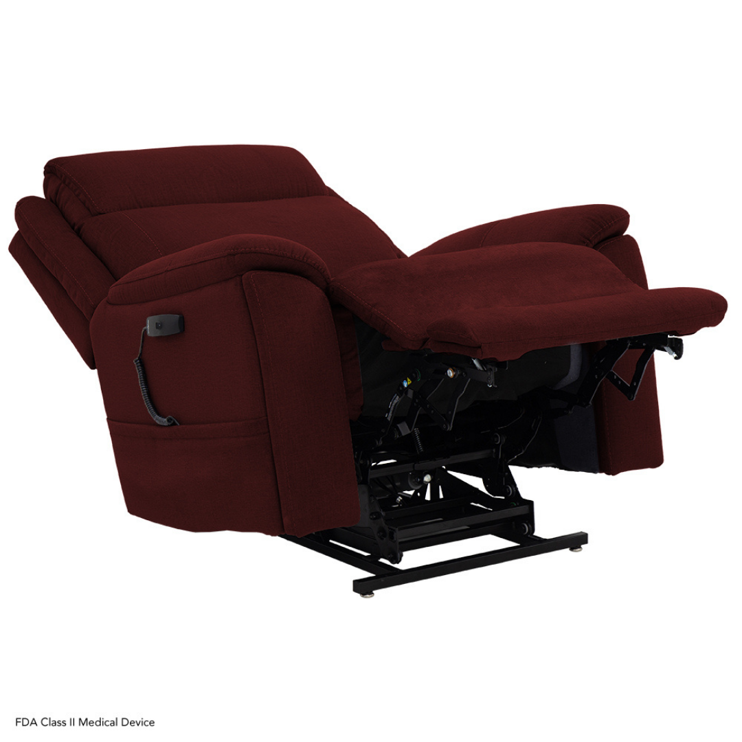 The Pride Mobility Evolution Collection Power Lift Recliner, upholstered in plush maroon fabric, is shown reclined with the footrest extended, revealing part of its lifting mechanism. A wired remote control is attached to the chair’s side.