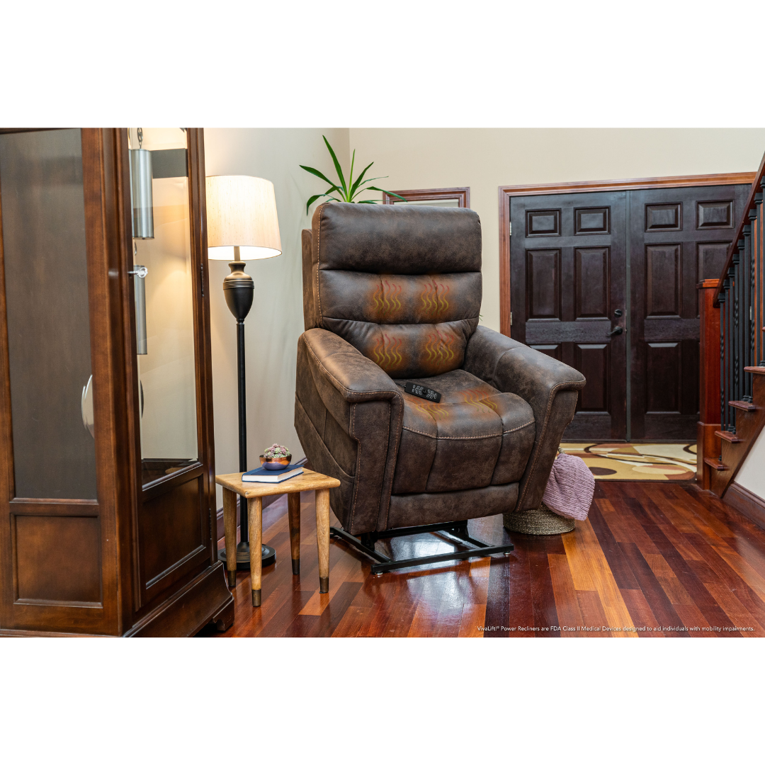 The Pride Mobility VivaLift! Radiance Recliner with Lift Assist & Heat, in a large brown design, sits on polished wood floors near a side table, lamp, and glass-front cabinet in a warmly lit entryway with double doors and a staircase.