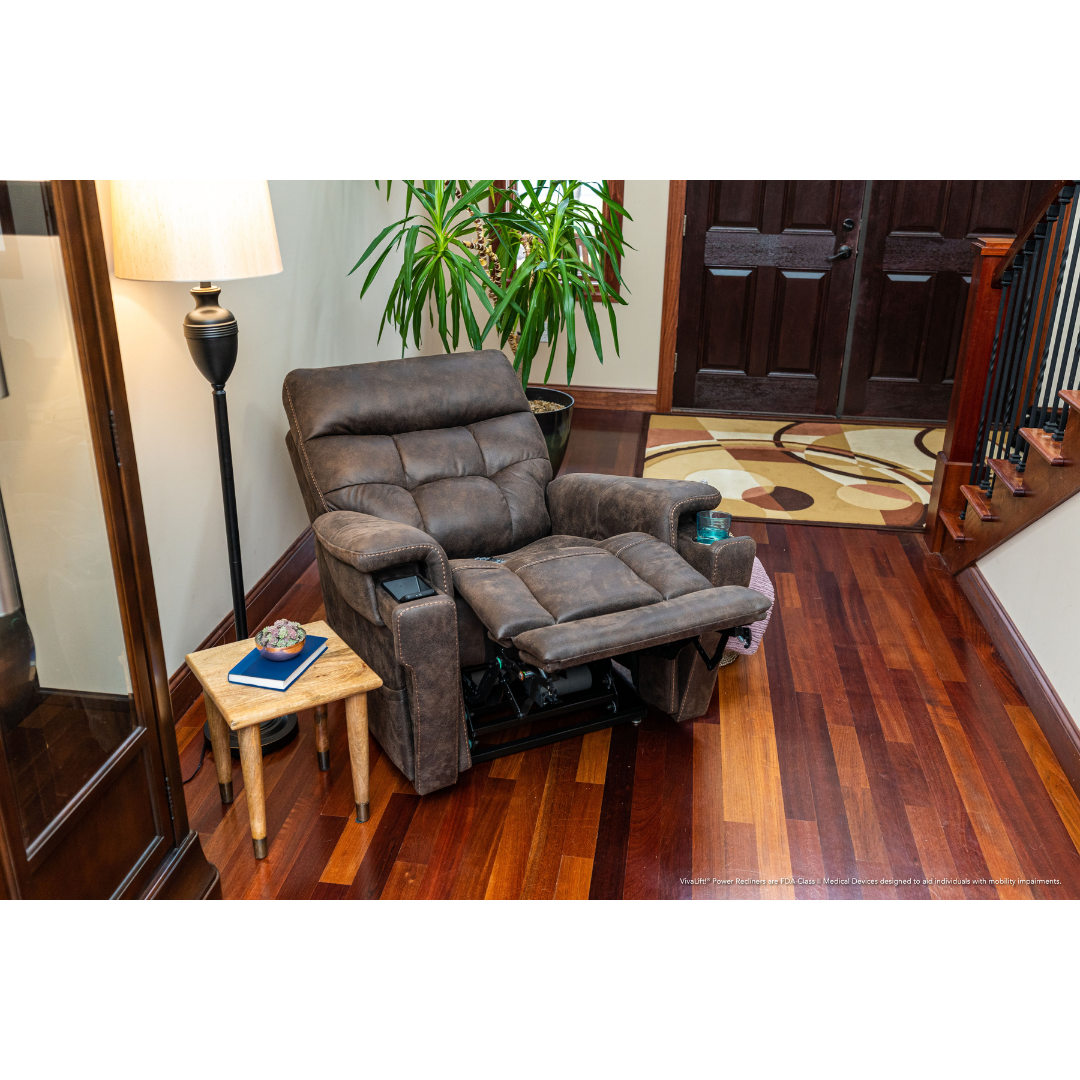 The Pride Mobility VivaLift! Radiance Recliner with Lift Assist & Heat, shown in brown with footrest extended on a wooden floor near a side table, lamp, and plant in a bright entryway, offers infinite positioning for ultimate comfort.