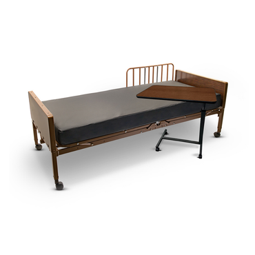 A hospital bed with a dark mattress and wooden headboard/footboard features a Proactive Medical Protekt Non-Tilt Overbed Table above it. The wheeled bed has a metal safety rail on one side.