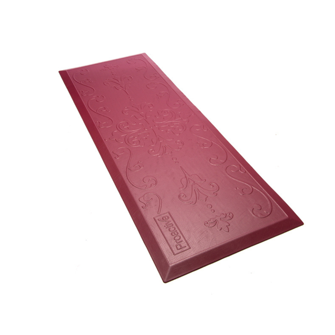 The Proactive Protekt® Beveled Fall Cushioned Floor Mat is a maroon mat with embossed floral patterns and the Prochi logo, shown on a white background. It’s designed as a low-profile fall mat for enhanced comfort and impact resistance.