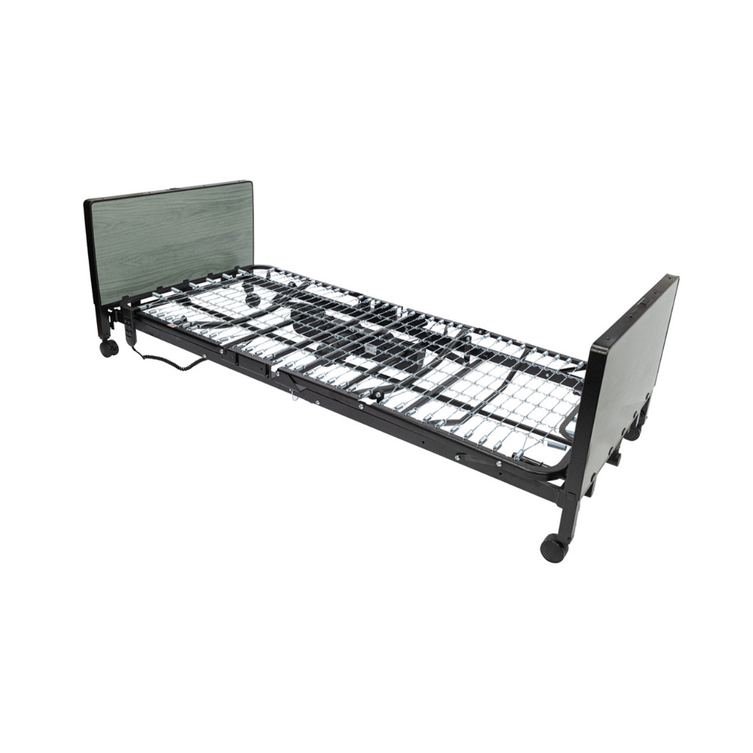 The Protekt Akra-FE™ Full-Electric Bariatric “Low” Bed features a sturdy metal frame, caster wheels, a wire grid base, and dark-colored head and footboards. The bed is displayed without a mattress in a neutral white setting.