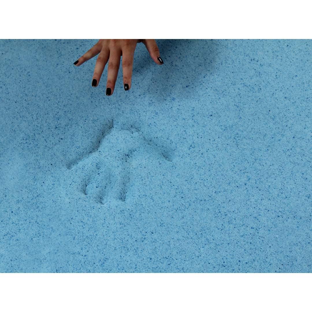 A hand with black-painted nails hovers above blue sand, next to a fresh handprint impressed into the surface—echoing the gentle relief and enduring comfort delivered by the Protekt® Geri-Chair Foam Overlay, expertly designed to cushion and support.