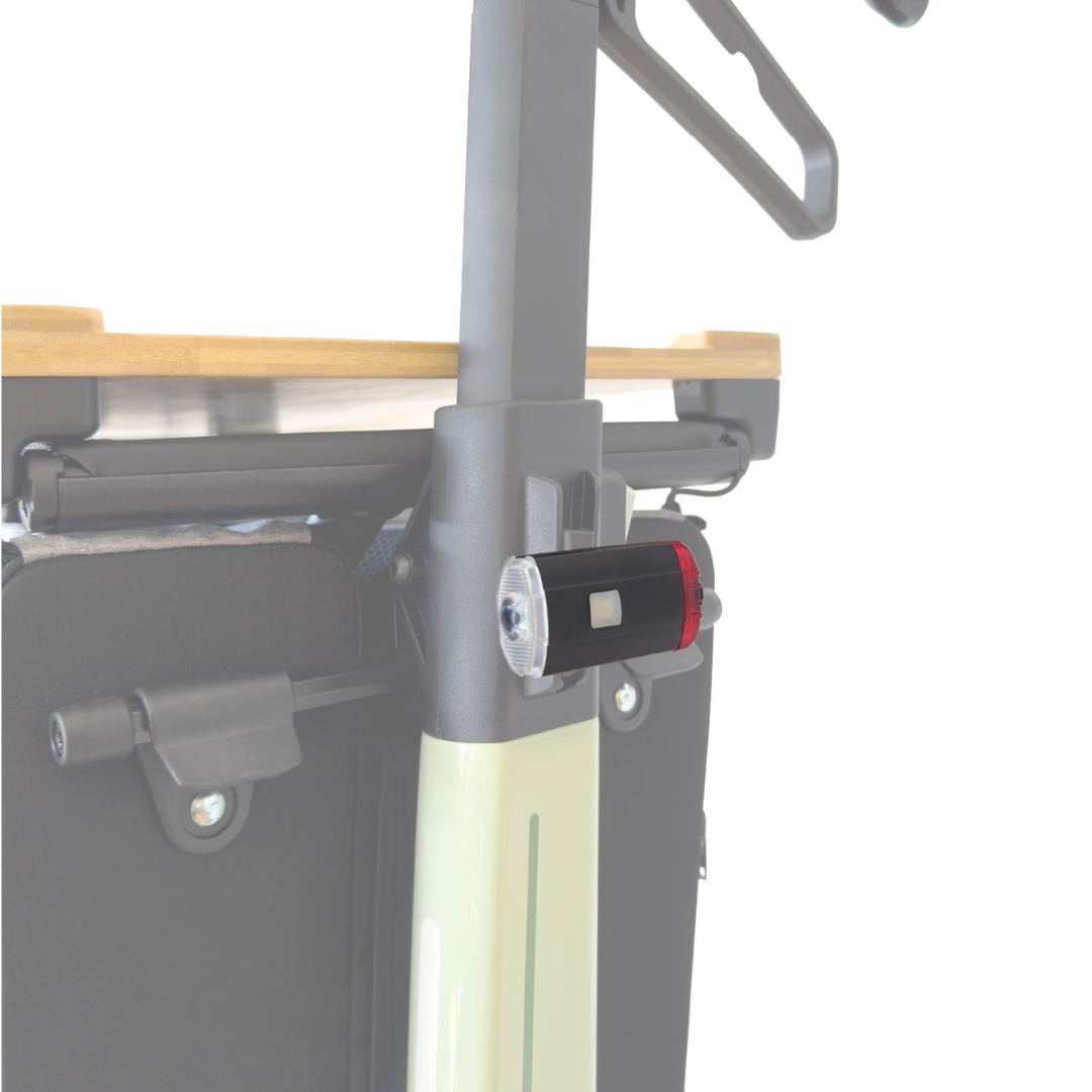 Close-up of the Light For The Rollz Air Rollator, an attachable black and red LED flashlight fixed to a Rollz Air Rollator’s pole, with a wooden surface and fabric bag in the background.