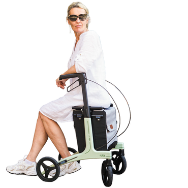 A woman in sunglasses and a white dress sits sideways on the Rollz Air Lightweight Folding Carbon Rollator (10.4 lbs) with large wheels and a storage bag, isolated on a white background.