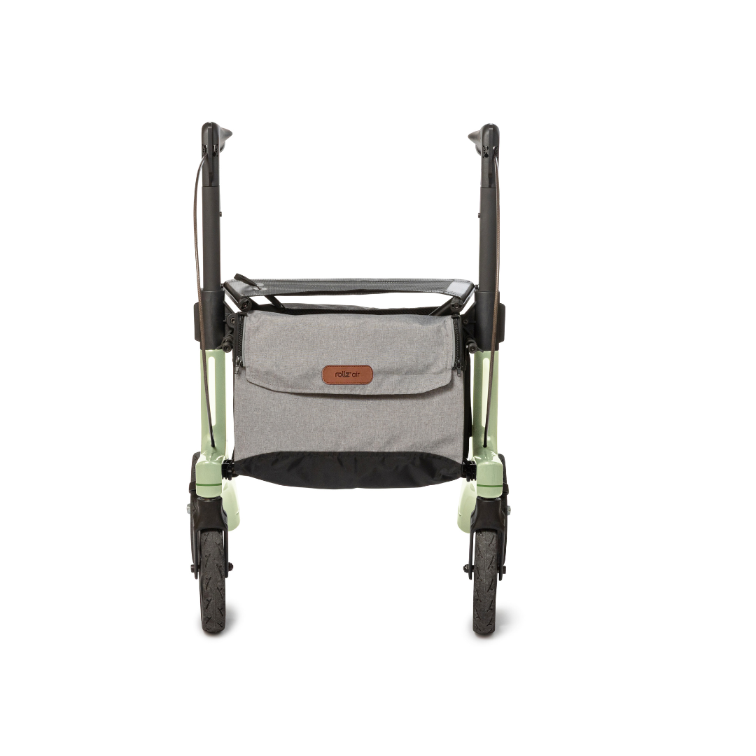 The image shows a front view of the Rollz Air Lightweight Folding Carbon Rollator (10.4 lbs) in green, featuring black handles, large front wheels, and a gray fabric storage bag attached to the front for convenience.