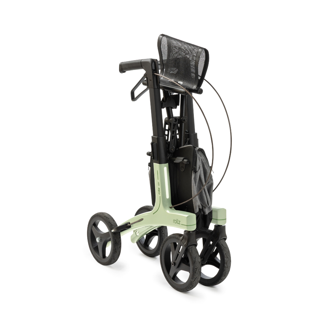 The Rollz Air Lightweight Folding Carbon Rollator, weighing just 10.4 lbs, is shown folded for storage or transport. It features a green and black design, four large wheels, and an attached mesh storage bag.