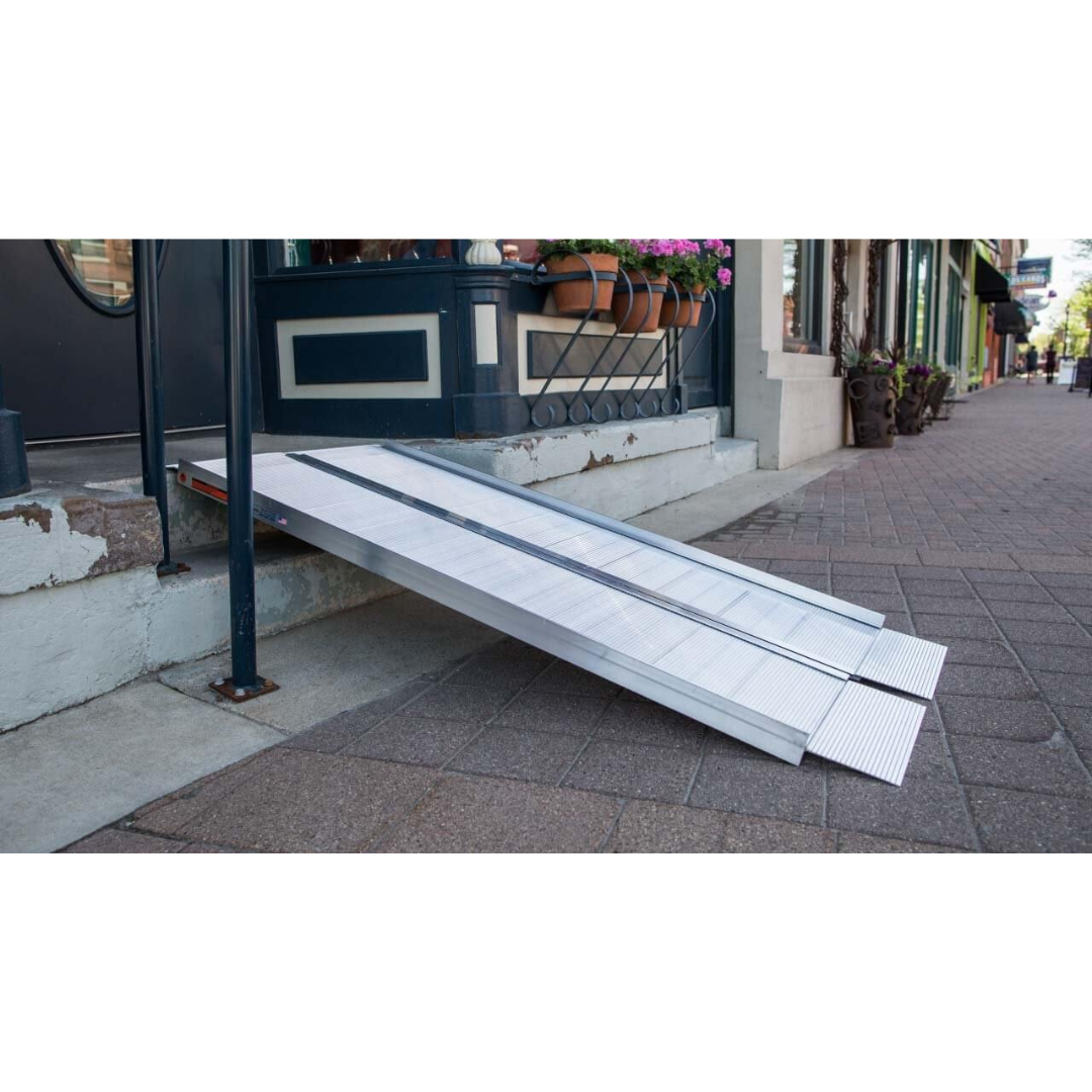 The EZ-Access SUITCASE® Singlefold Mobility Ramp - Portable is set up on a sidewalk, giving access over steps to a storefront. Interested customers can view videos and warranty details about its features and specifications.