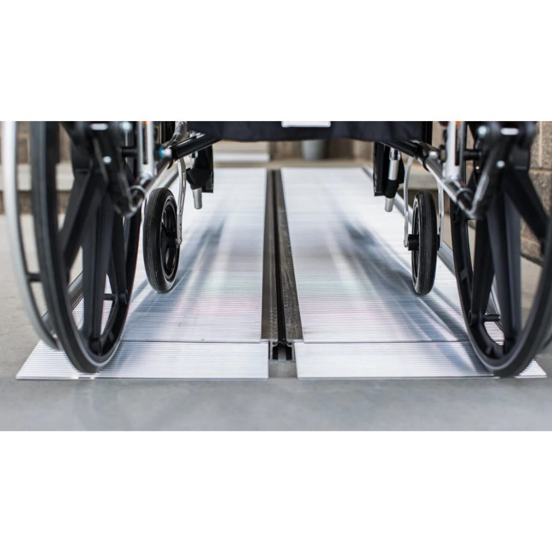 Close-up of a wheelchair on the EZ-Access SUITCASE® Singlefold Mobility Ramp - Portable, leading over a threshold. The low-angle view showcases the ramp’s sturdy aluminum construction and quality, backed by warranty.