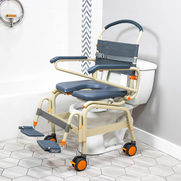 The ShowerBuddy SB6C Bariatric Rolling Shower Chair, with padding, armrests, footrests, and wheels, is shown over a toilet in a modern bathroom featuring hexagonal floor tiles and a white bathtub.