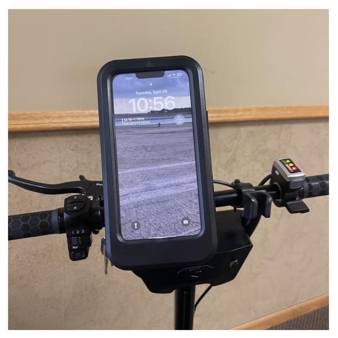A smartphone, displaying 10:56 on Tuesday, April 30, is mounted on a Glion SNAPnGO Scooters handlebars in a black holder. The dashboard and control buttons are visible, powered by a lithium-ion battery.
