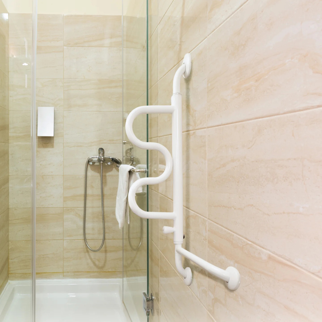 Accessible shower with beige tiled walls, glass door, showerhead, and a white towel on the faucet. Features the Stander Curve Grab Bar - 180° Pivoting Arm for bathroom safety.