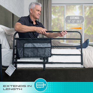 A man sits on a bed adjusting the Stander Wonder Pivot Bed Safety Rail - Tall with a mesh pocket. An arrow and text indicate the rail extends to 26", 32", and 38.5" for nighttime safety. Bottom text: Extends in length.