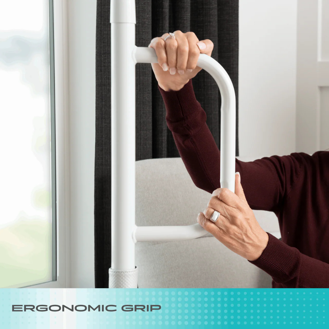 A person in a maroon sweater grips a Stander Wonder Pole Lite fall prevention safety pole by a window, with "ERGONOMIC GRIP" text at the bottom.