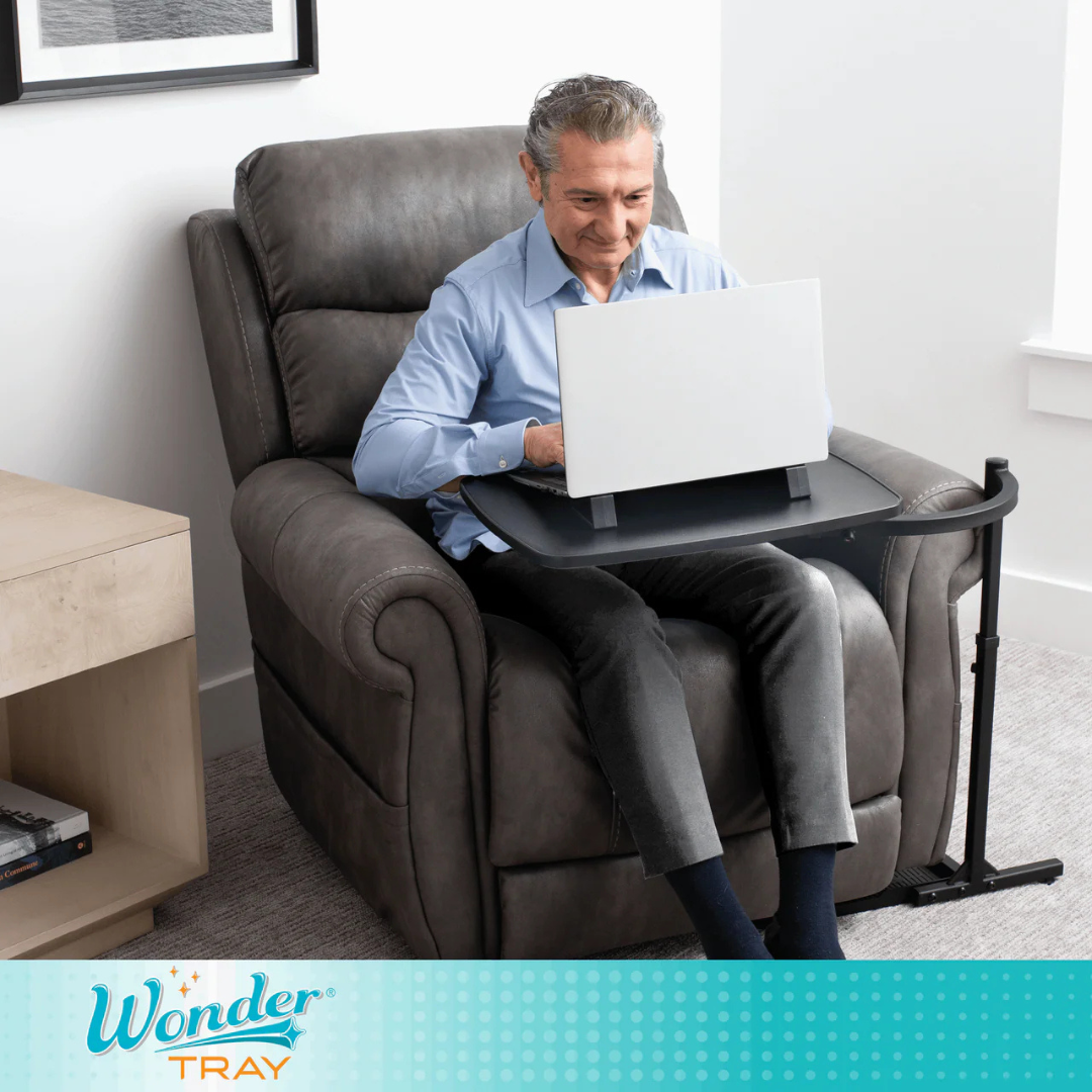 An older man relaxes in a gray recliner, using his laptop on the Stander Wonder Tray - Swivel Living Room Tray Table. The black adjustable tray serves as a perfect laptop stand in the bright, modern room, where he looks focused and content.