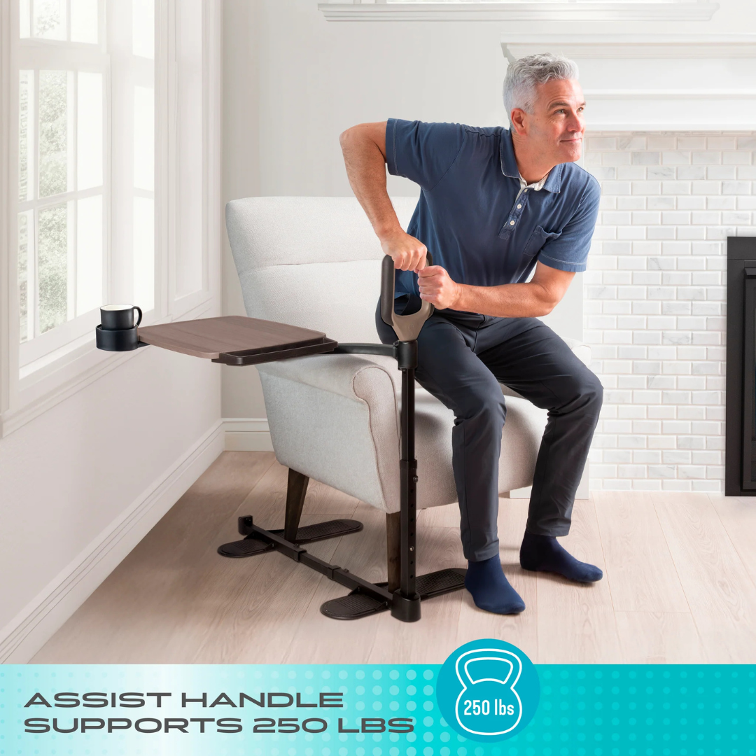 A man uses the Stander Wonder Tray Premium - XL TV Tray & Standing Aid, attached to a chair and side table, to help himself stand up (supports up to 250 lbs). A cup sits on the tray, and the chair is near a white brick fireplace.