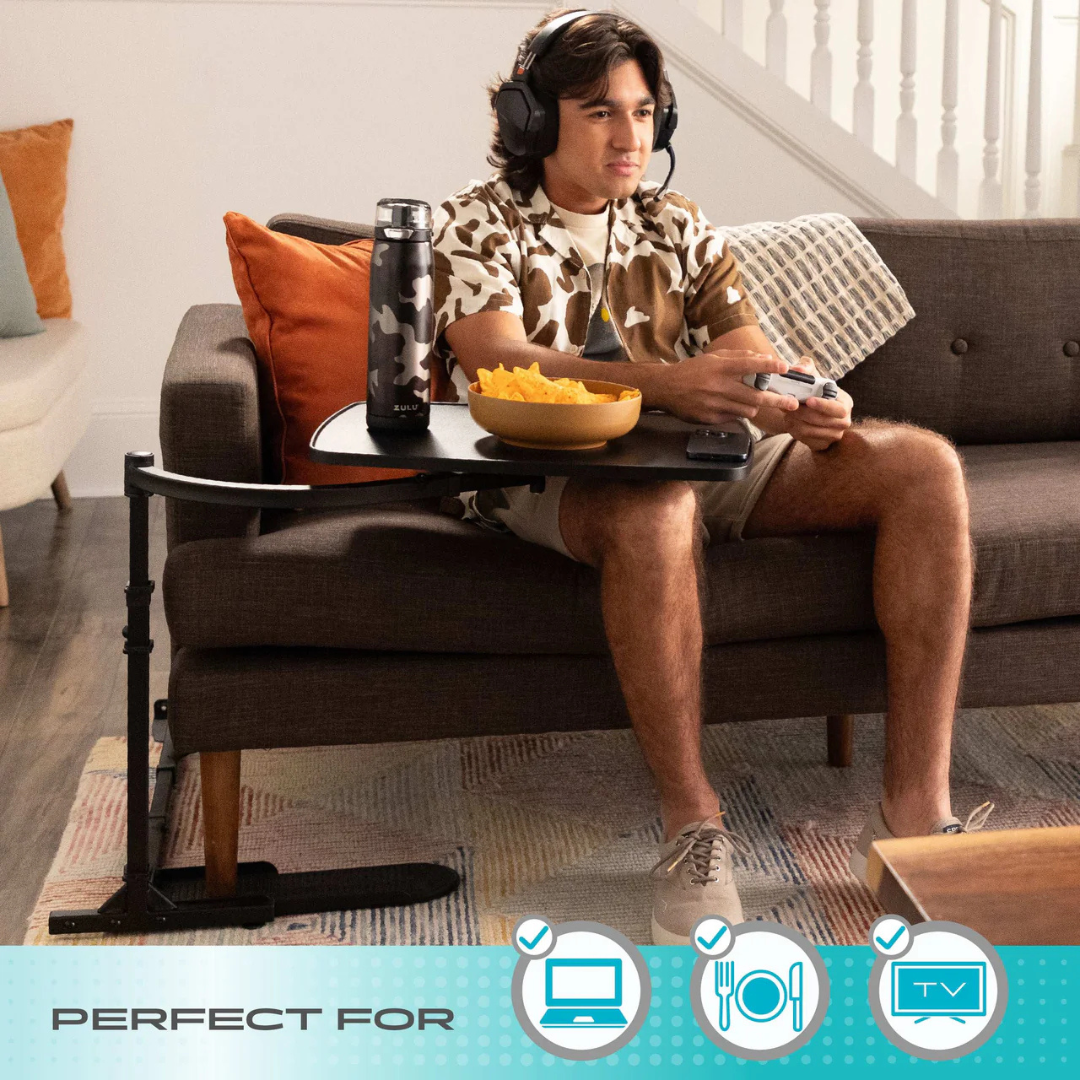 A young man wearing headphones plays video games on a couch, using the Stander Wonder Tray—Swivel Living Room Tray Table to hold chips, a drink, and a remote in his cozy living room. The versatile tray is ideal for multi-purpose use.