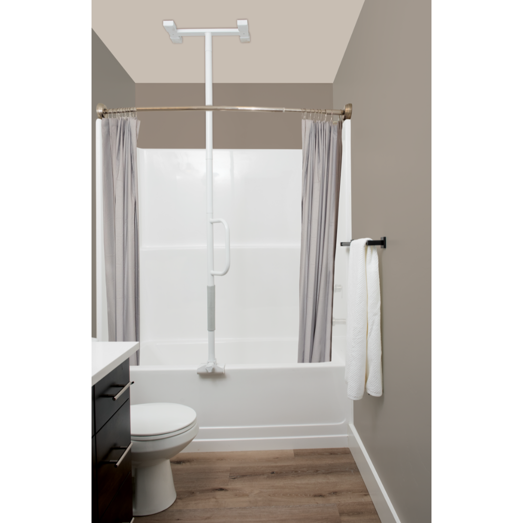 A safe bathroom with a bathtub and shower, Stander Wonder Bathtub Pole Lite for support, sturdy grab bar, gray curtains, white toilet, towels on a rack, and brown wood-style flooring.