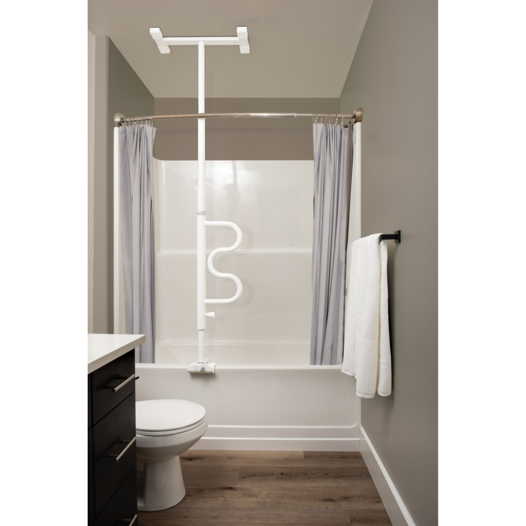 A bathroom with a white bathtub, curved shower rod and gray curtains, a Stander Wonder Bathtub Pole over the tub for fall prevention, a toilet, wall rack towel, and wood-style flooring.
