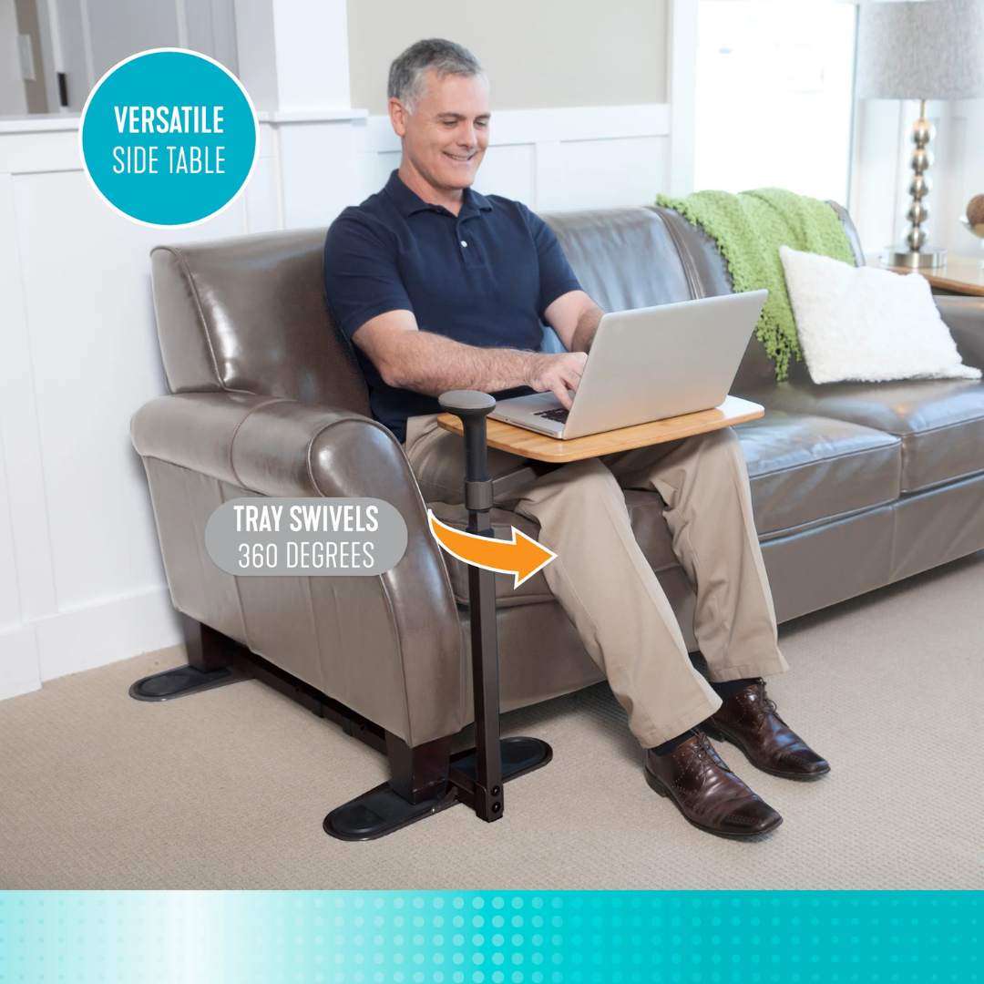 A smiling man uses his laptop on the Stander Omni Tray – TV Tray & Standing Aid, attached to a brown sofa. The side table has a black metal frame and swivels 360° for convenience. Text reads VERSATILE SIDE TABLE.