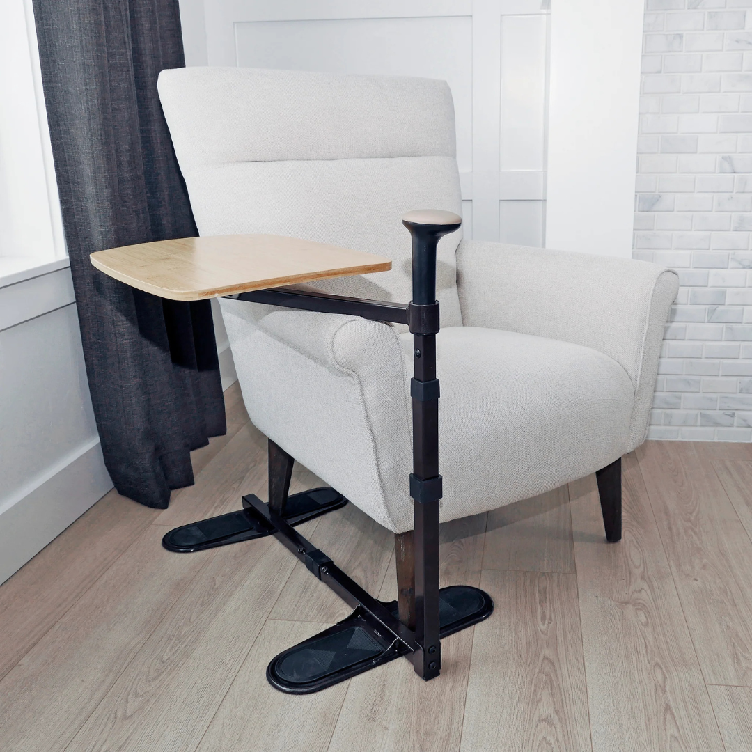 The Stander Omni Tray – TV Tray & Standing Aid, featuring a support handle and swiveling wooden tray, is placed near a window with dark curtains and light wood floors, adding comfort and functionality to your living space.