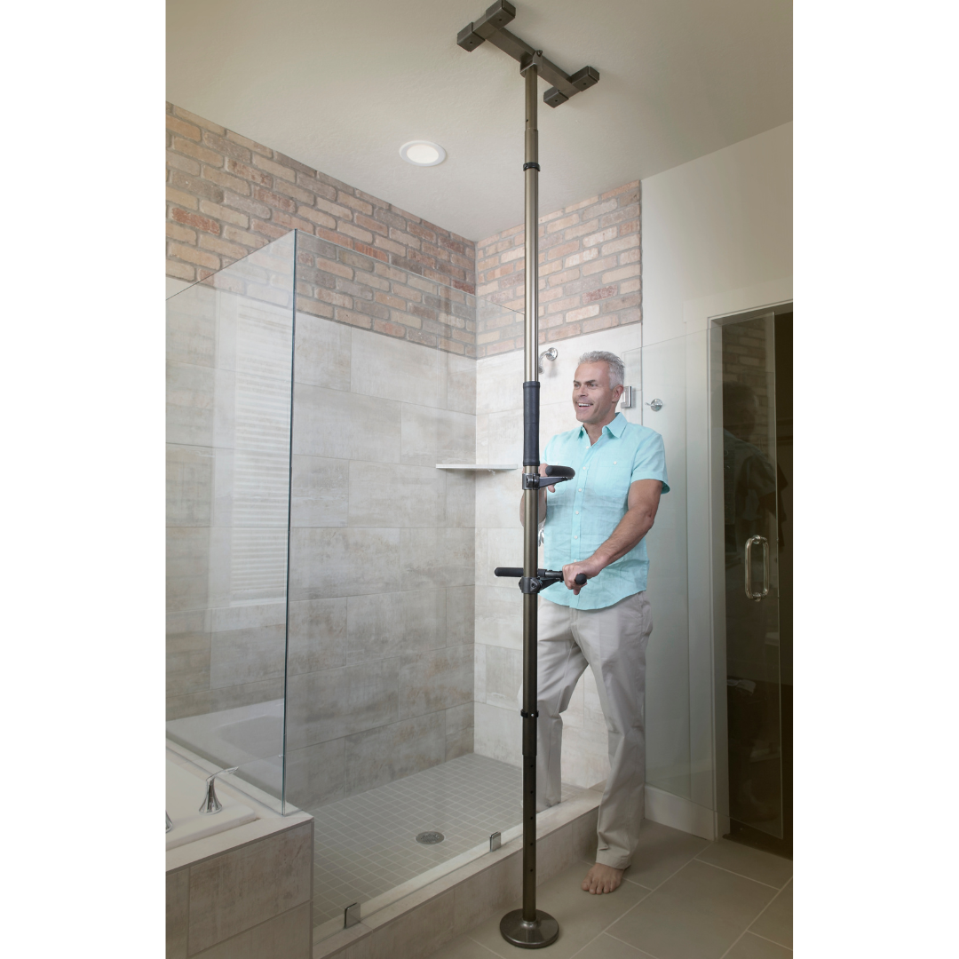 A man stands in a modern, tiled shower with a glass door and brick accent wall, using the Stander Wonder Pole Premium - Fall Prevention Pole - Universal Fit for added bathroom safety and stability.