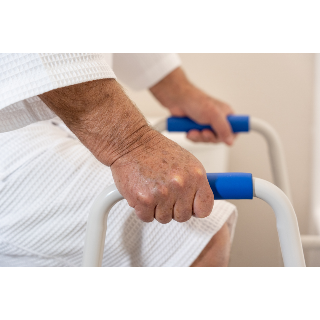 Close-up of an elderly person gripping blue handles on the Step2Tub Bathtub Step Stool while using it as a mobility aid near the bedside, wearing a white robe for added fall prevention.