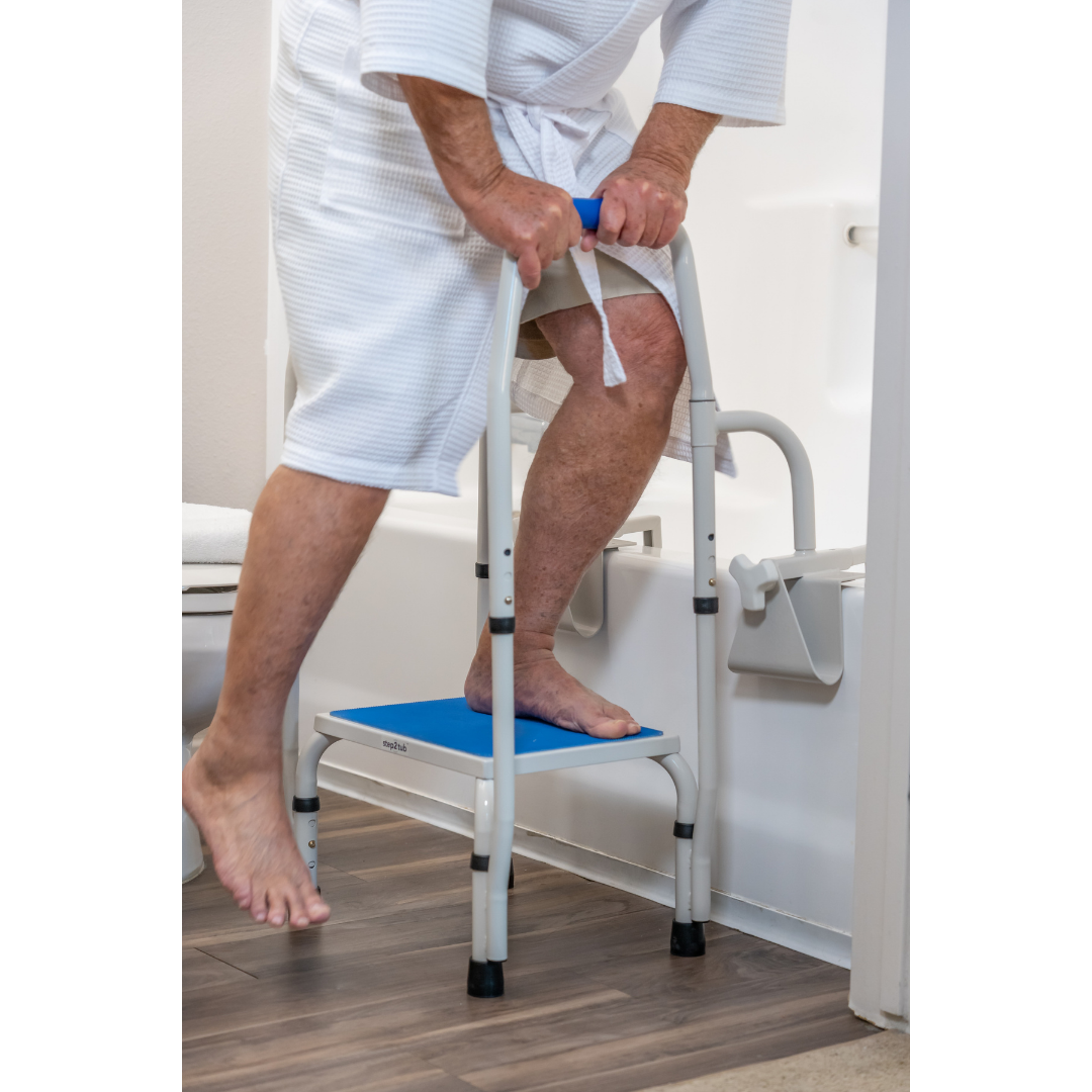An older adult in a bathrobe uses the Step2Tub Bathtub Step Stool with handrails to safely step into the bathtub, demonstrating fall prevention and improved bathroom access.