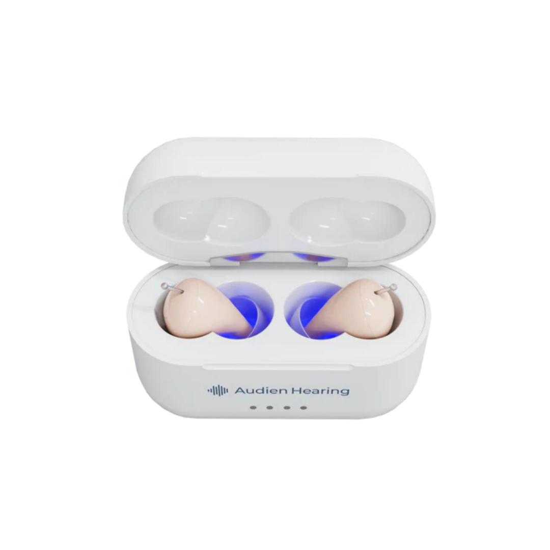 A white Audien Hearing Atom Pro 2 In-Ear OTC Hearing Aids case with the lid open displays two beige hearing aids lit by blue light. The case has the Audien logo, three front indicator lights, and advanced hearing modes powered by the A2™ chip.