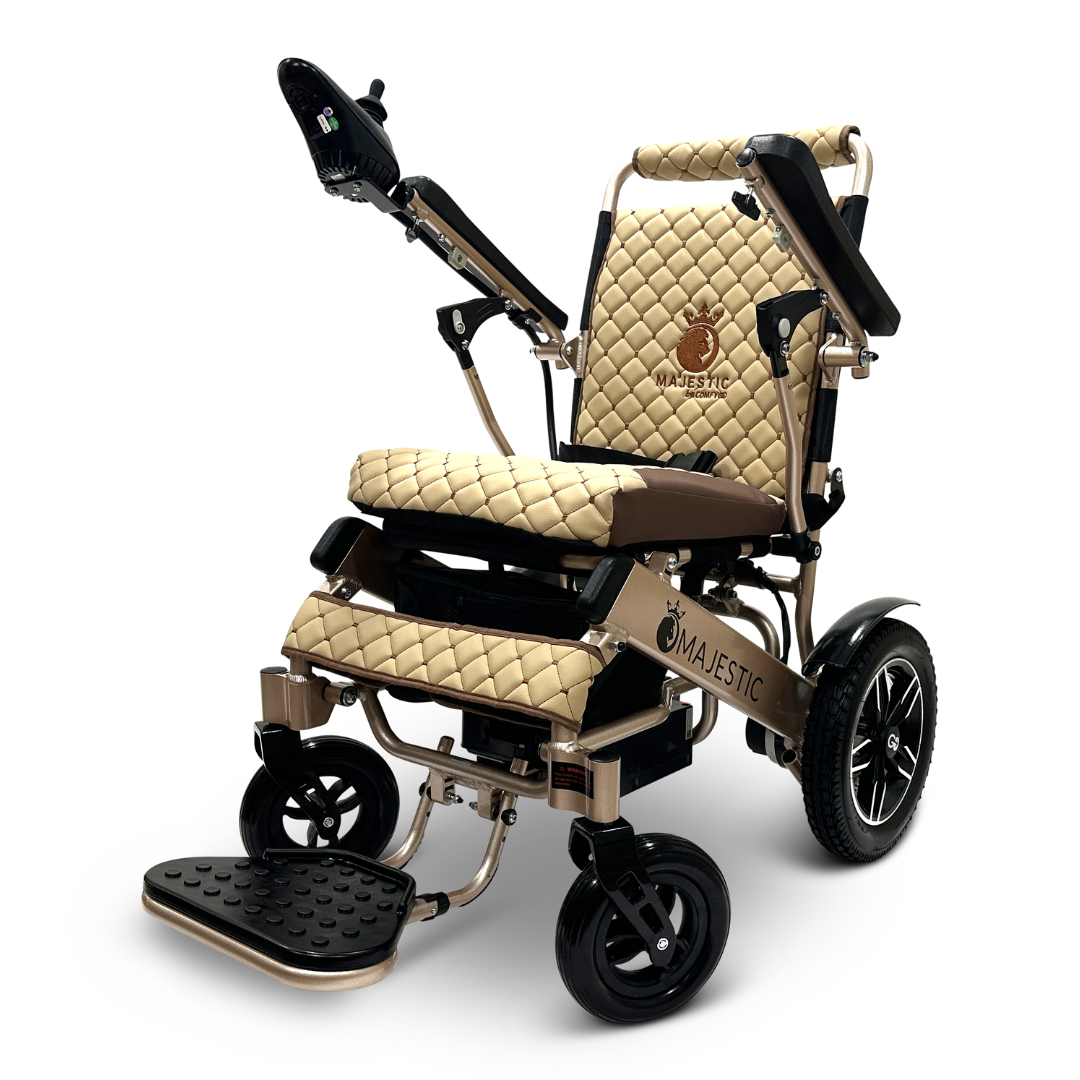 The ComfyGo MAJESTIC IQ-8000 Remote Controlled Lightweight Electric Wheelchair features a quilted design with a joystick control located on the armrest. It includes large rear wheels, smaller front wheels, and provides comfort with its cushioned seat and backrest. The wheelchair's metallic frame is adorned with Majestic branding and a horse logo, combining style with travel convenience.