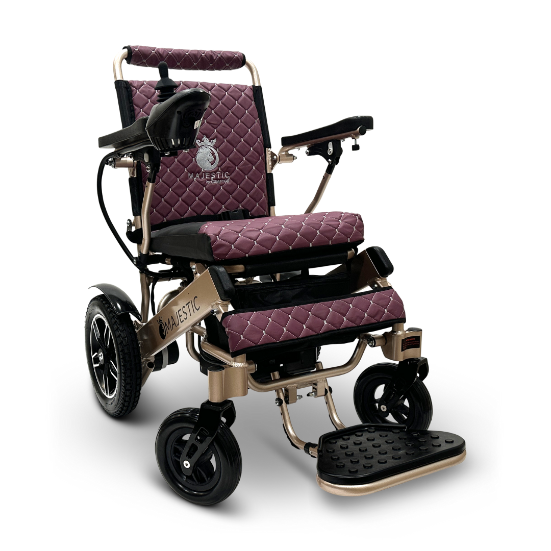 The ComfyGo MAJESTIC IQ-8000 Remote Controlled Lightweight Electric Wheelchair is designed in purple with a quilted pattern. It features large rear wheels, smaller front wheels, and black footrests. Its lightweight metallic frame makes it perfect for travel, and the chair is equipped with armrests that include control mechanisms on the left side.