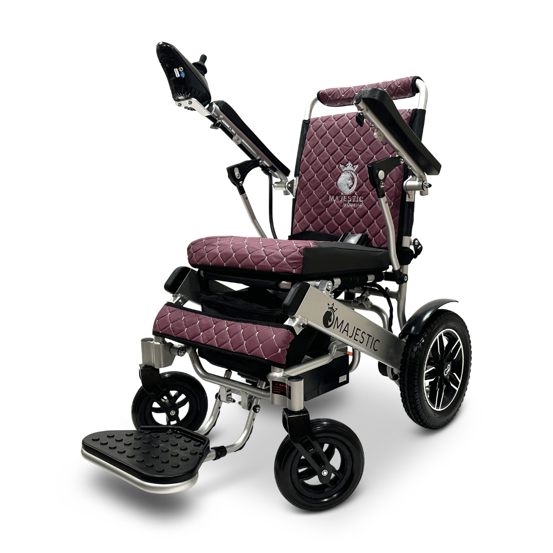 The ComfyGo MAJESTIC IQ-8000 Remote Controlled Lightweight Electric Wheelchair is designed for travel convenience, featuring a quilted burgundy seat and backrest, a modern silver frame, and stylish black accents. It includes large rear wheels, smaller front wheels, a footrest, and an intuitive armrest joystick for easy navigation.