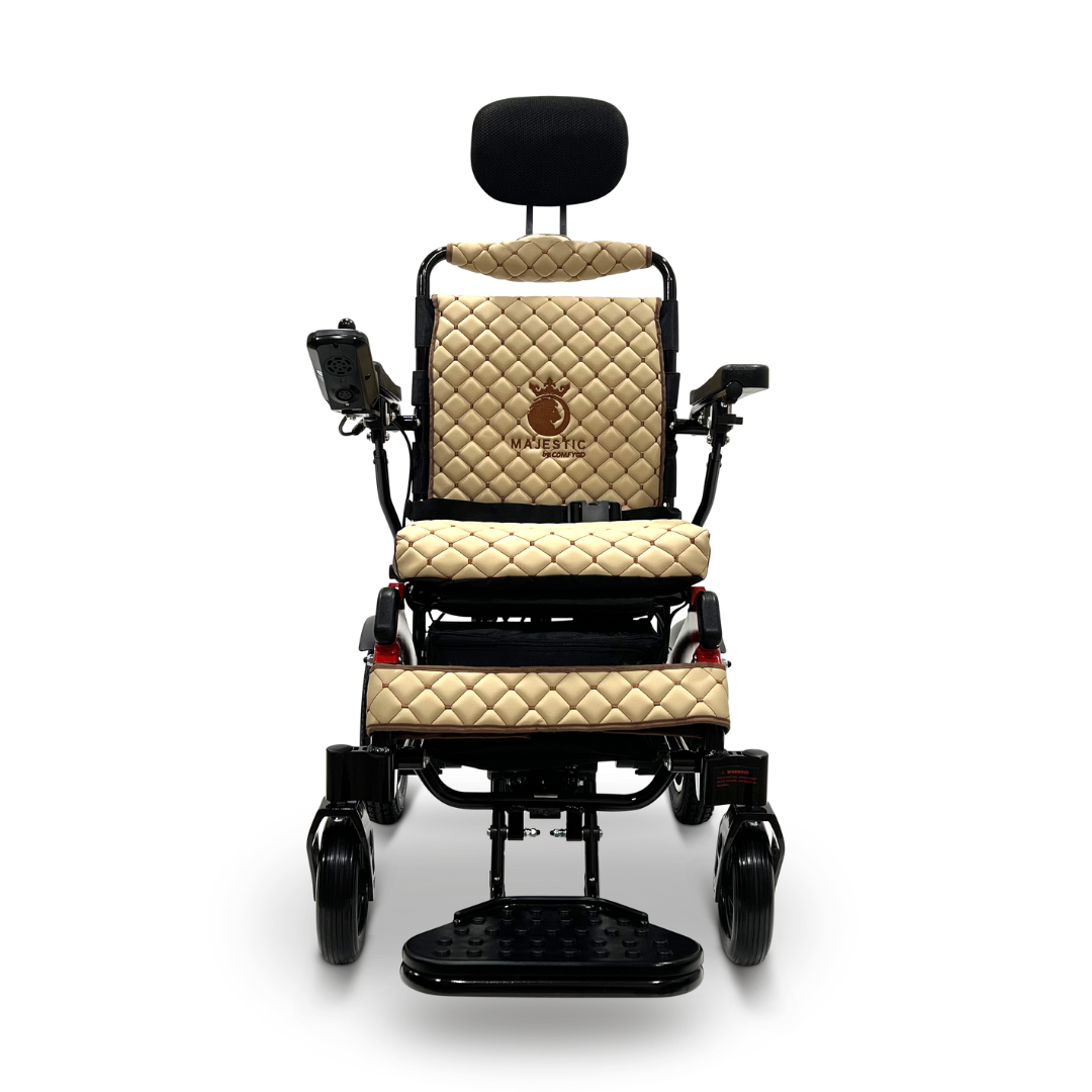 The front view displays the ComfyGo MAJESTIC IQ-9000 Auto Recline Remote Controlled Electric Wheelchair, featuring a tan quilted design with a high backrest and headrest. It includes a digital joystick controller on the right armrest, black footrests, and has the Majestic brand name embroidered on the backrest. The wheelchair is powered by brushless silent motors for smooth operation.