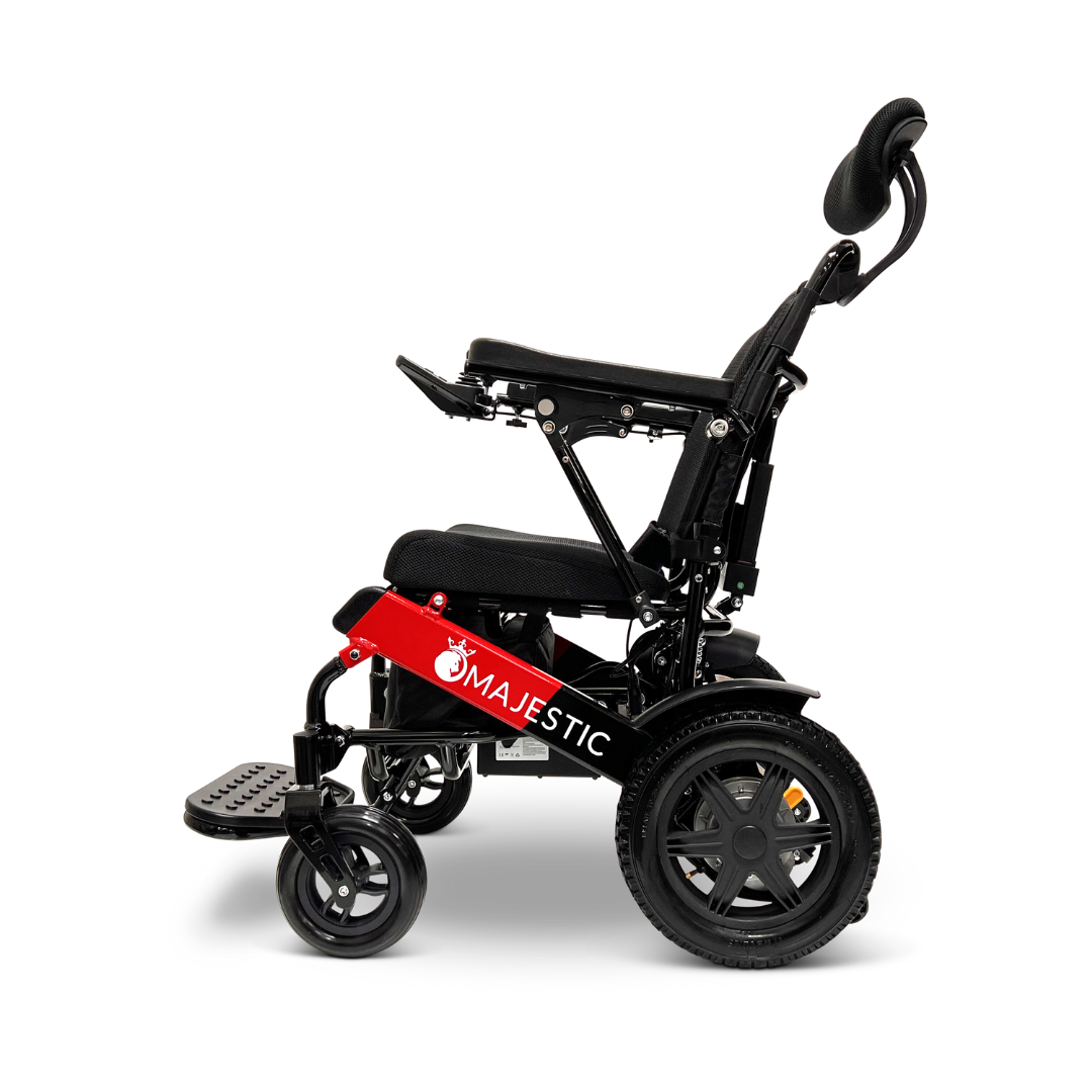 Side view of a folded black and red ComfyGo MAJESTIC IQ-9000 Auto Recline Remote Controlled Electric Wheelchair with the word MAJESTIC printed on the side. It features brushless silent motors, a cushioned seat and backrest, adjustable armrests and footrests, and a digital joystick controller for seamless control.