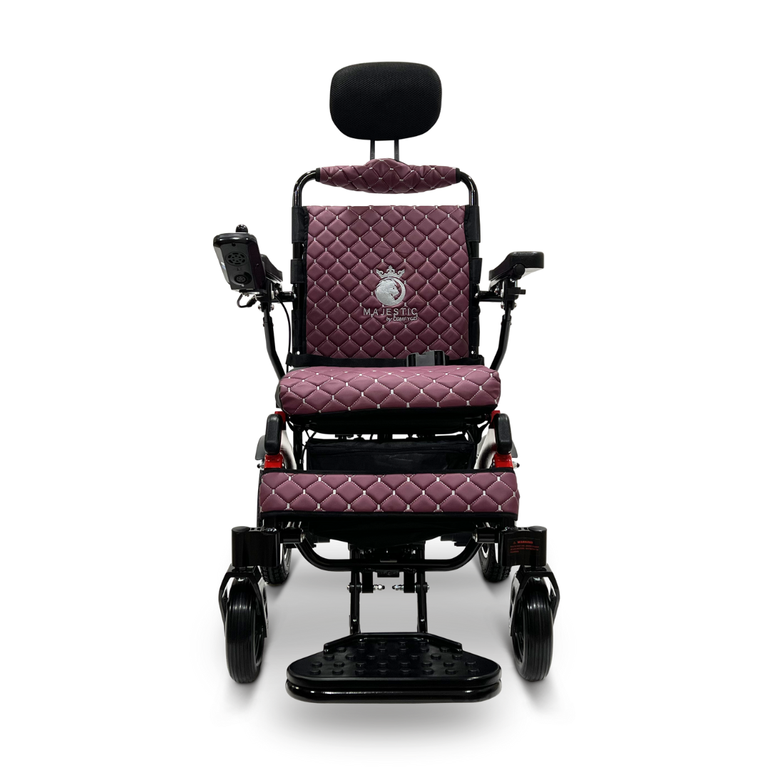 The ComfyGo MAJESTIC IQ-9000 Auto Recline Remote Controlled Electric Wheelchair in maroon features quilted cushions, black armrests, a comfortable headrest, and a digital joystick controller for smooth maneuvering. Equipped with brushless silent motors for a noiseless experience, this wheelchair also includes sturdy black wheels and a logo-adorned backrest for an elegant look.