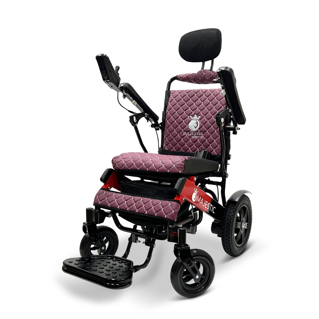 The ComfyGo MAJESTIC IQ-9000 Auto Recline Remote Controlled Electric Wheelchair features a quilted maroon seat, armrests, and a black headrest. It is equipped with brushless silent motors and a digital joystick controller on the right armrest. The wheelchair also includes four wheels, a footrest, and prominently displays "Majestic" on its frame.