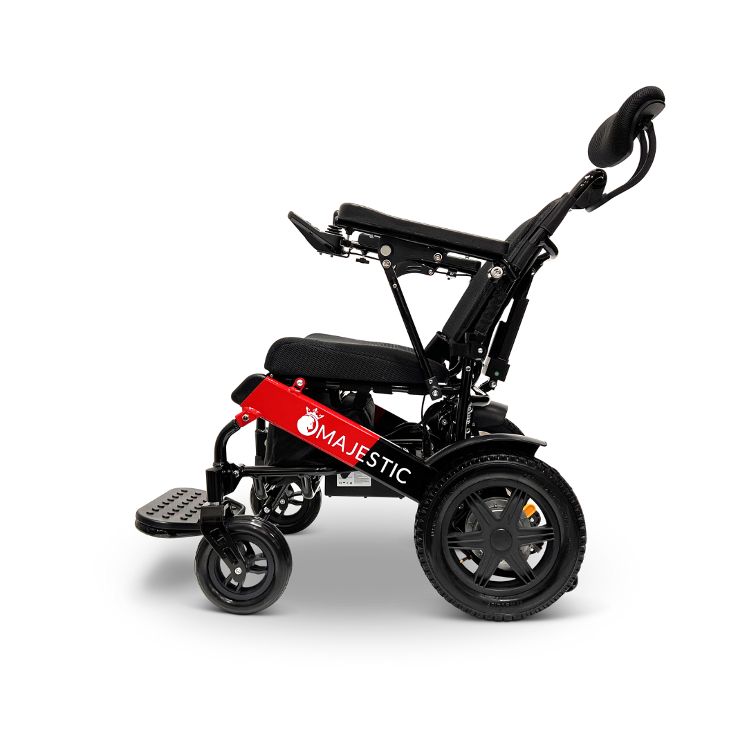 A side view of the ComfyGo MAJESTIC IQ-9000 Auto Recline Remote Controlled Electric Wheelchair highlights its sleek black and red design with distinctive MAJESTIC branding. Featuring brushless silent motors, it includes padded seating, a headrest, and footrests. The digital joystick controller provides smooth maneuverability while the large rear wheels enhance comfort.